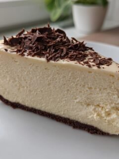 A decadent slice of Baileys Cheesecake, topped with chocolate shavings, on a white plate.