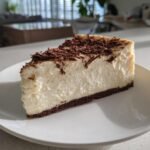 A delicious slice of Baileys Cheesecake topped with chocolate shavings on a white plate.