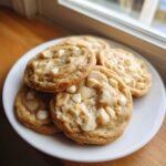 A close-up of freshly baked Bakery Style White Chocolate Macadamia Cookies piled on a white plate.