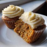 Two Carrot Cake Cupcakes With Cream Cheese Frosting, one cut open to show the moist interior with visible carrots.