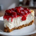 A close-up shot of a thick slice of creamy Cherry Cheesecake topped with glossy, bright red cherries.