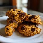 A stack of delicious Chocolate Chip Pumpkin Oatmeal Cookies on a white plate, with one cookie broken in half.
