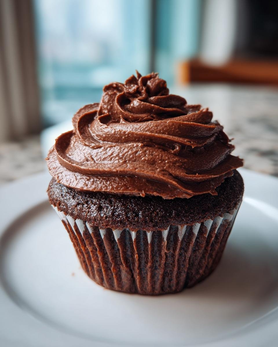 A close-up of a dark chocolate cupcake topped with a generous swirl of rich Nutella Frosting.