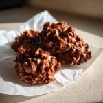 Four rich, dark mounds of Chocolate Peanut Butter No Bake Cookies studded with oats, resting on white parchment paper.