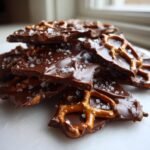 A close-up stack of broken pieces of rich Chocolate Pretzel Bark topped with flaky sea salt.
