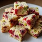 Close-up of stacked squares of Cranberry Pistachio Shortbread, studded with red cranberries and green pistachios, topped with sugar.