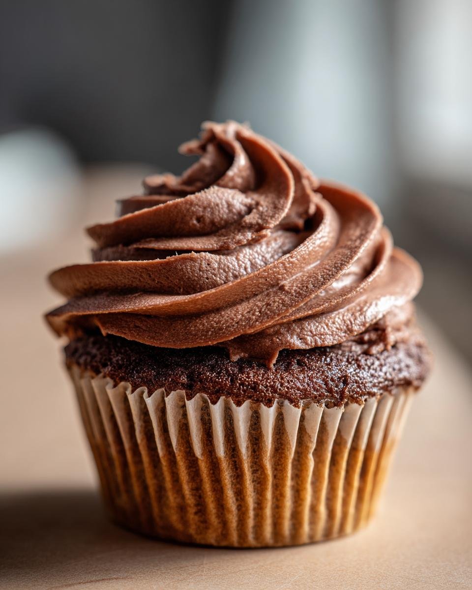 Close-up of a chocolate cupcake topped with a thick, perfectly piped swirl of Nutella Frosting.