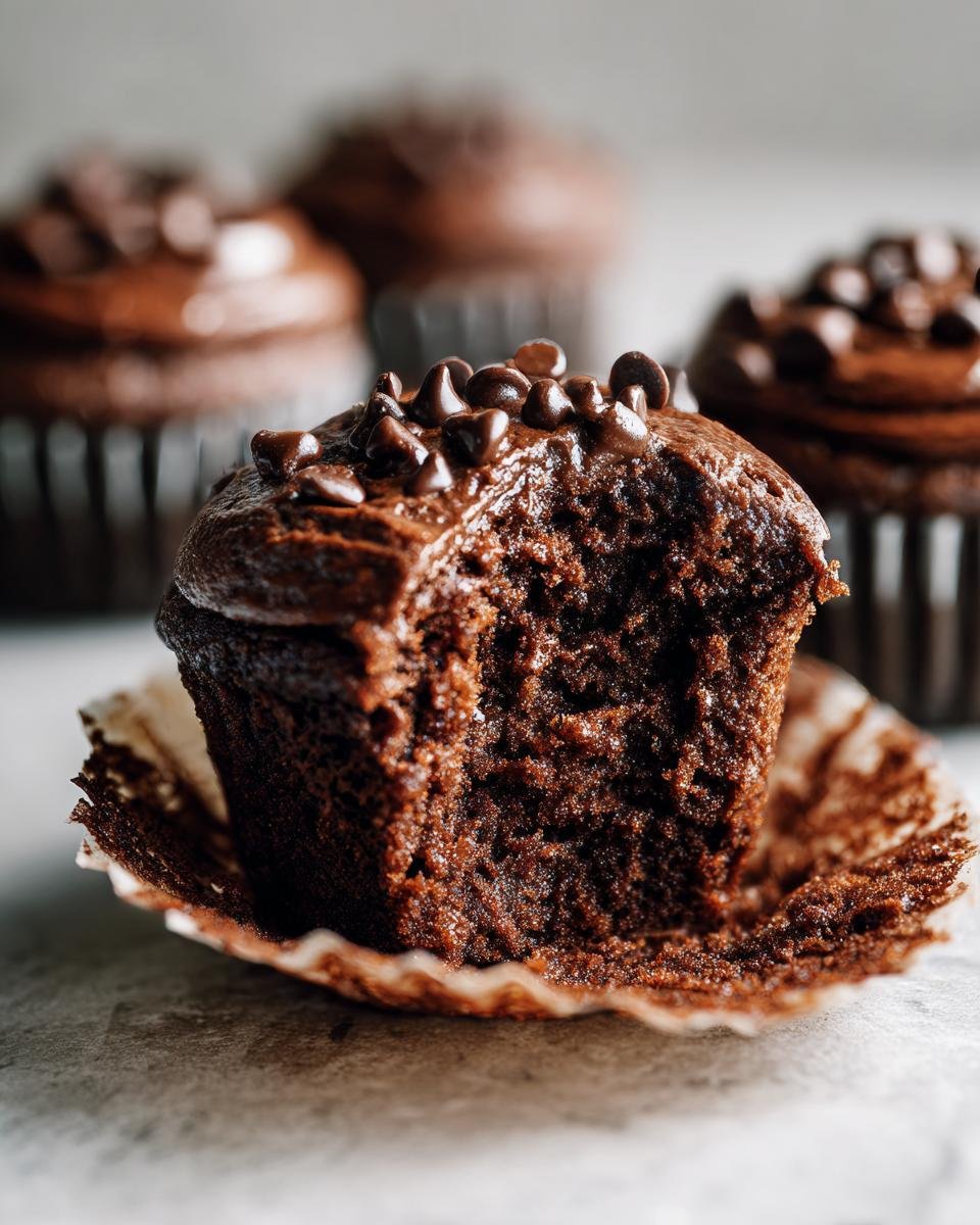 A close-up of a Double Chocolate Banana Cupcake with a bite taken out, showing moist crumb and chocolate chips.