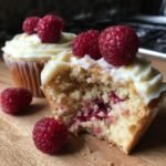Close-up of a Lemon Raspberry Cupcake, showing the moist interior with raspberries and white frosting topped with fresh raspberries.