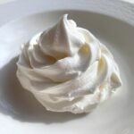 A swirl of fluffy white frosting, perfect for cakes and desserts, showcasing the ease of how to make white frosting.
