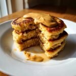 A stack of fluffy Minute Peanut Butter Banana Pancakes cut in half, topped with melted peanut butter.