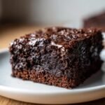 Close-up of a moist, dark, fudgy square of Chocolate Slice on a white plate.