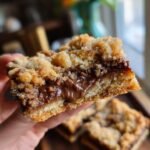A hand holds a delicious Nutella Crumb Bar, revealing a gooey chocolate Nutella filling between crumbly layers.