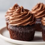 A close-up of a dark chocolate cupcake topped with a generous swirl of Nutella frosting, part of a batch of Nutella Cupcakes.