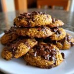 A close-up stack of delicious Pumpkin Chocolate Chip Cookies, generously topped with melted chocolate chips.
