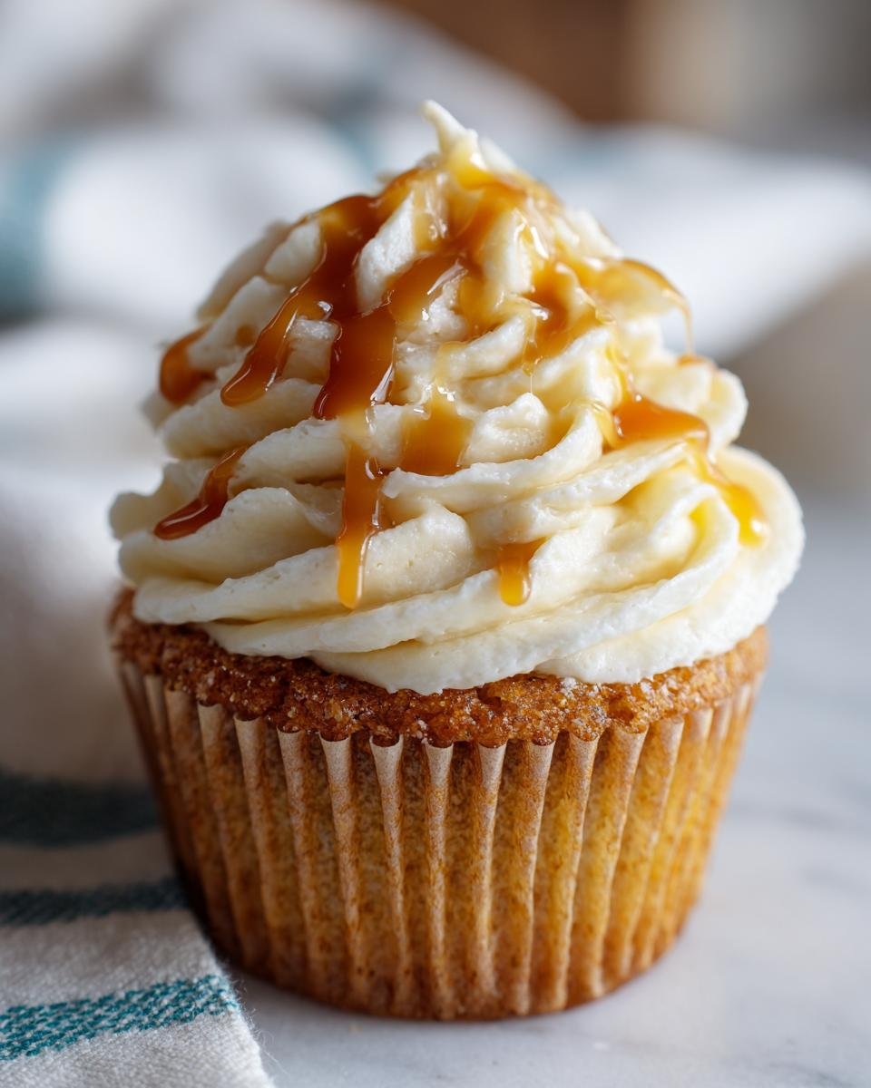 A delicious Pumpkin Cupcake topped with swirls of Caramel Cream Cheese Frosting and drizzled with caramel sauce.