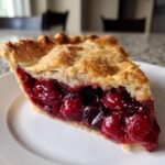 A close-up of a thick slice of homemade Cherry Pie showing juicy filling and flaky, sugared crust.