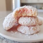 Stack of soft Strawberry Cookies heavily dusted in powdered sugar, with the top cookie broken open showing pink strawberry bits inside.