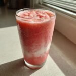 A tall glass filled with a vibrant, icy Strawberry Banana Smoothie, catching bright sunlight.
