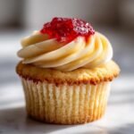 A close-up of a delicious Strawberry Lemonade Cupcake with creamy frosting and a dollop of red jam.