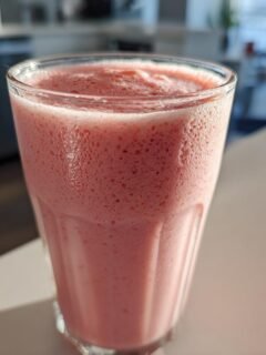 A close-up of a frothy, pink Strawberry Milkshake served in a ribbed glass on a bright countertop.