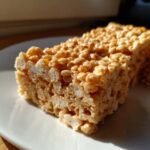 Close-up of a delicious Tiger Bars Butterscotch Rice Krispie Treat on a white plate, showing the texture of puffed rice and melted butterscotch.