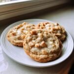 Three freshly baked White Chocolate Macadamia Cookies with melted white chocolate chunks on a white plate.