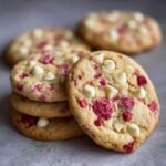 A close-up stack of freshly baked White Chocolate Raspberry Cookies, showcasing white chocolate chips and vibrant raspberry pieces.