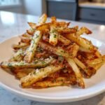 A mound of golden, crispy Air Fryer Garlic Herb Yucca Fries seasoned with parsley and Parmesan cheese.