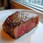 Close-up of a medium-rare Air Fryer Steak, perfectly seared and seasoned with salt and pepper.