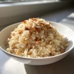 A white bowl filled with fluffy Almond Brown Rice Pilaf, generously topped with toasted sliced almonds.