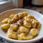 A white bowl filled with The Best Cacio E Pepe Gnocchi coated in a creamy cheese sauce and heavily topped with cracked black pepper.