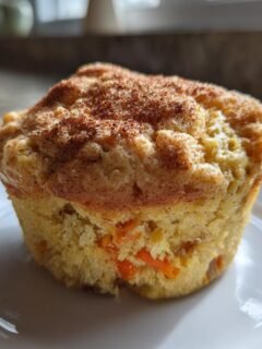 A single, freshly baked Carrot Breakfast Muffin topped with cinnamon, sitting on a white plate.