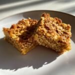 Two freshly baked, chewy Oatmeal Bars with a golden, crunchy oat topping resting on a white plate.