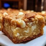A close-up shot of a thick, chewy White Chocolate Blondies square with visible white chocolate chips.