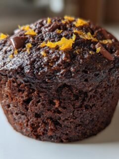 A single, dark, rich Chocolate Orange Muffins, topped with chocolate chips and bright orange zest.