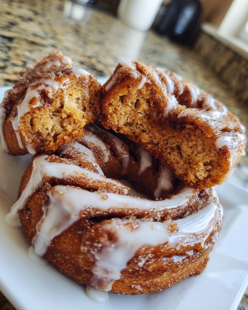 Close-up of two Cinnamon Roll Donuts, one broken open to show the soft, spiced interior and thick white glaze.