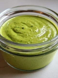 A close-up of bright green, thick Creamy Cilantro Lime Dressing in a small glass jar.