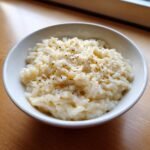 A close-up of Irresistible Creamy Garlic Parmesan Rice topped with grated cheese and black pepper in a white bowl.
