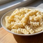 Close-up of fusilli pasta coated in a thick, creamy sauce in a white bowl, representing Creamy Hummus Pasta.