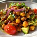Close-up of a vibrant Creamy Roasted Chickpeas And Avocado Salad topped with red onion and cilantro.