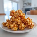 A close-up of crunchy Caramel Corn clusters generously coated in golden caramel sauce, served on a white plate.