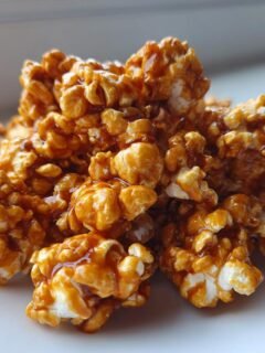 A pile of golden brown, glossy Caramel Corn clusters coated in rich caramel sauce on a white plate.