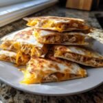 A stack of golden-brown, freshly cooked chicken quesadilla triangles overflowing with melted cheddar cheese.