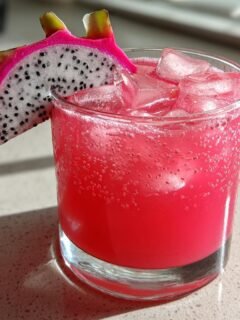 A vibrant pink Dragonfruit Pineapple Smash Mocktail served over ice, garnished with a slice of white dragonfruit.