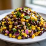 A close-up of vibrant Easy Black Bean Salsa piled high on a white plate, featuring black beans, yellow corn, and diced red onion.