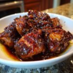 Close-up of rich, dark, glossy pieces of Easy Chicken Adobo swimming in sauce in a white bowl.