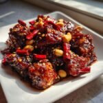 Close-up of glossy, saucy Easy Kung Pao Chicken pieces garnished with whole peanuts and dried red chilies.