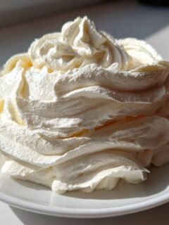 A beautiful swirl of stiff, white Vanilla Frosting piped high onto a small white plate, catching bright sunlight.