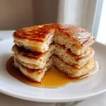 A tall stack of fluffy Almond Flour Pancakes drizzled generously with maple syrup.